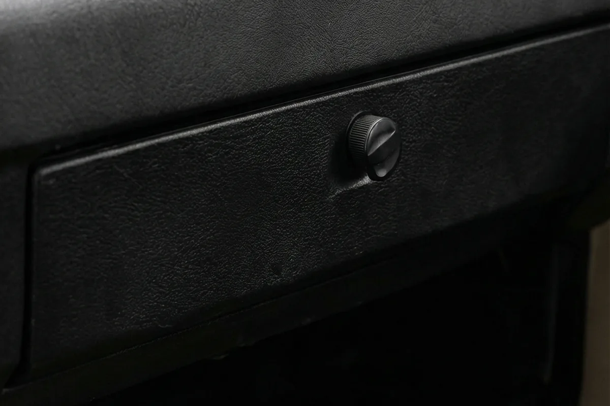 Detalhe de um botão preto giratório em um painel escuro e texturizado dentro do Fiat 147 City Sandstorm.