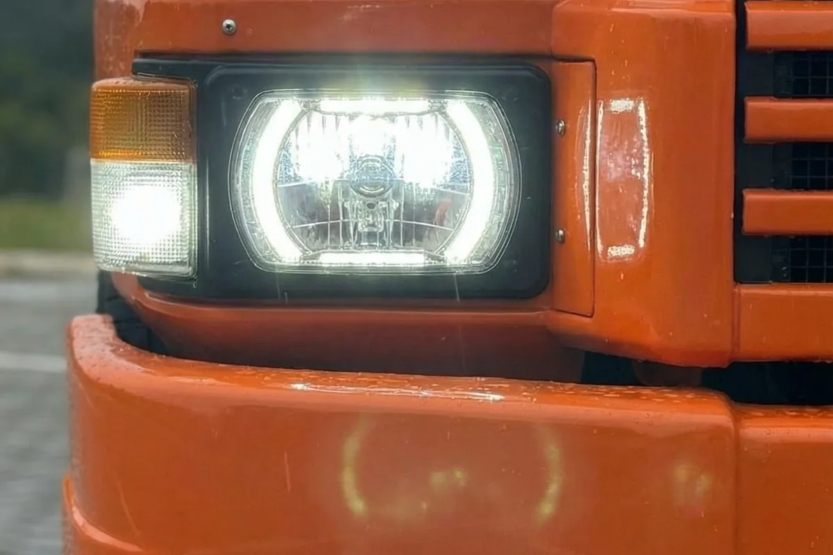 Close-up do farol dianteiro esquerdo do Fuscania 112H, um LED quadrado com DRL halo e pisca âmbar.