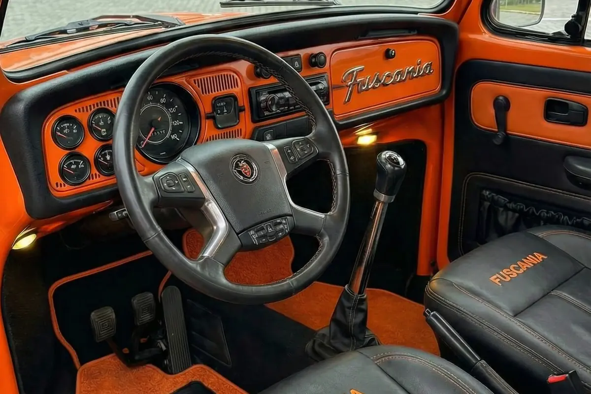 Interior do Fuscania 112H em laranja e preto, com painel customizado, volante moderno e bancos.