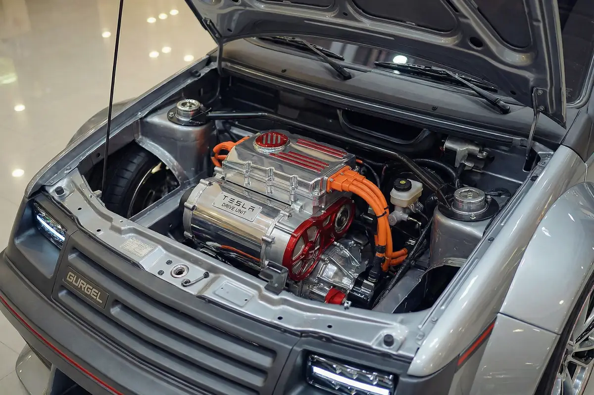 Motor elétrico Tesla Drive Unit cromado com cabos laranja e detalhes vermelhos no compartimento do Gurgel BR800.