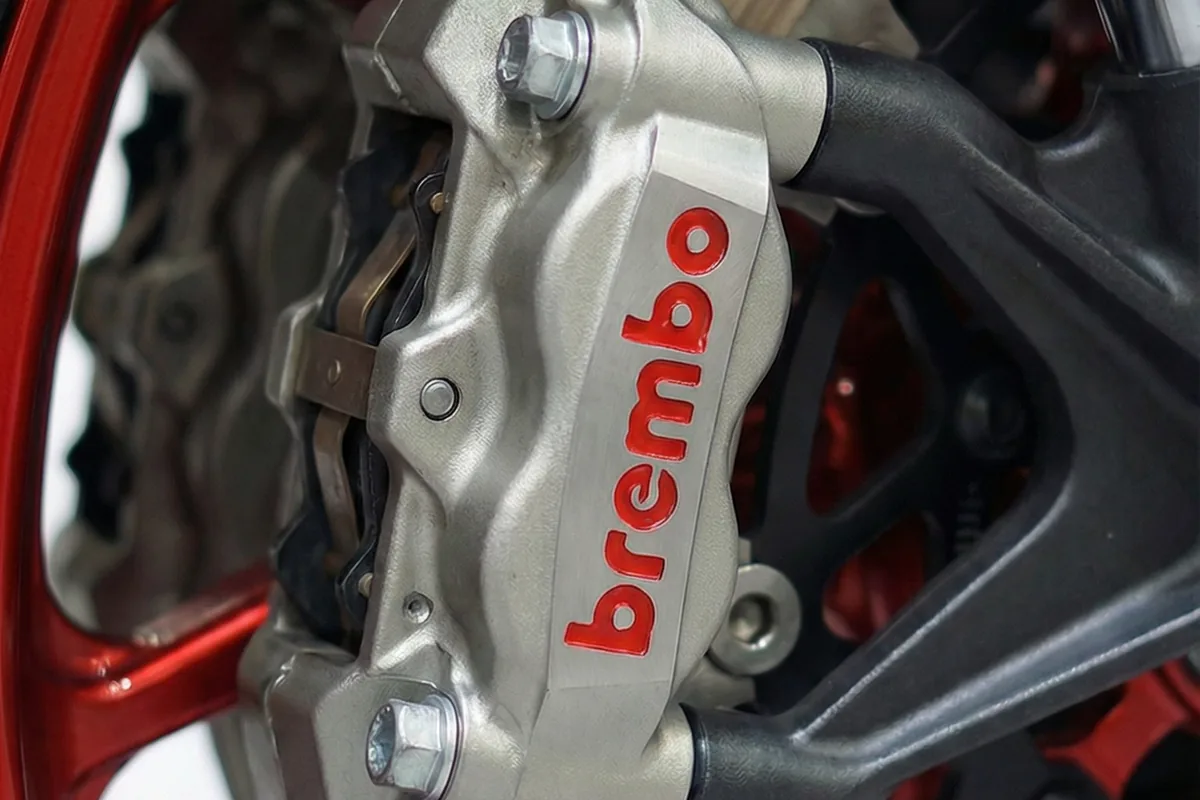 Close-up da pinça de freio Brembo prateada com logo vermelho, em destaque, próxima à roda vermelha da RD350.