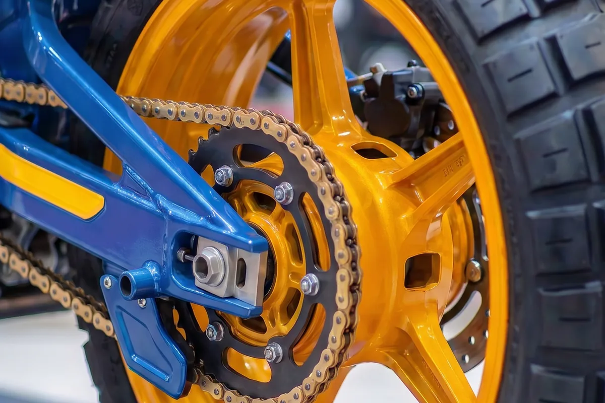 Close-up da roda traseira dourada, corrente e coroa da Yamaha Tenere 600 Concept, braço oscilante azul.
