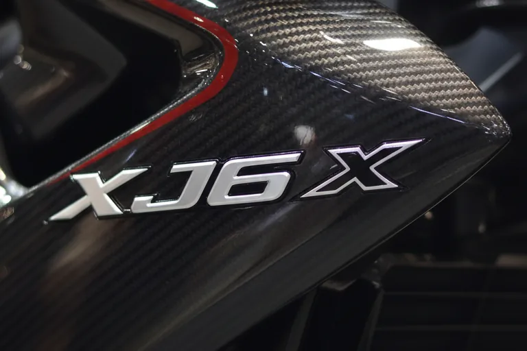 Close-up da carenagem lateral em fibra de carbono com emblema XJ6 X cromado e friso vermelho
