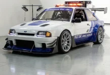 Escort XR3 Pace Car: o hatch mais desejado dos anos 80 numa recriação por IA Ford Escort XR3 em conceito pace car, branco e azul, visto em três quartos dianteiro num galão de piso polido.