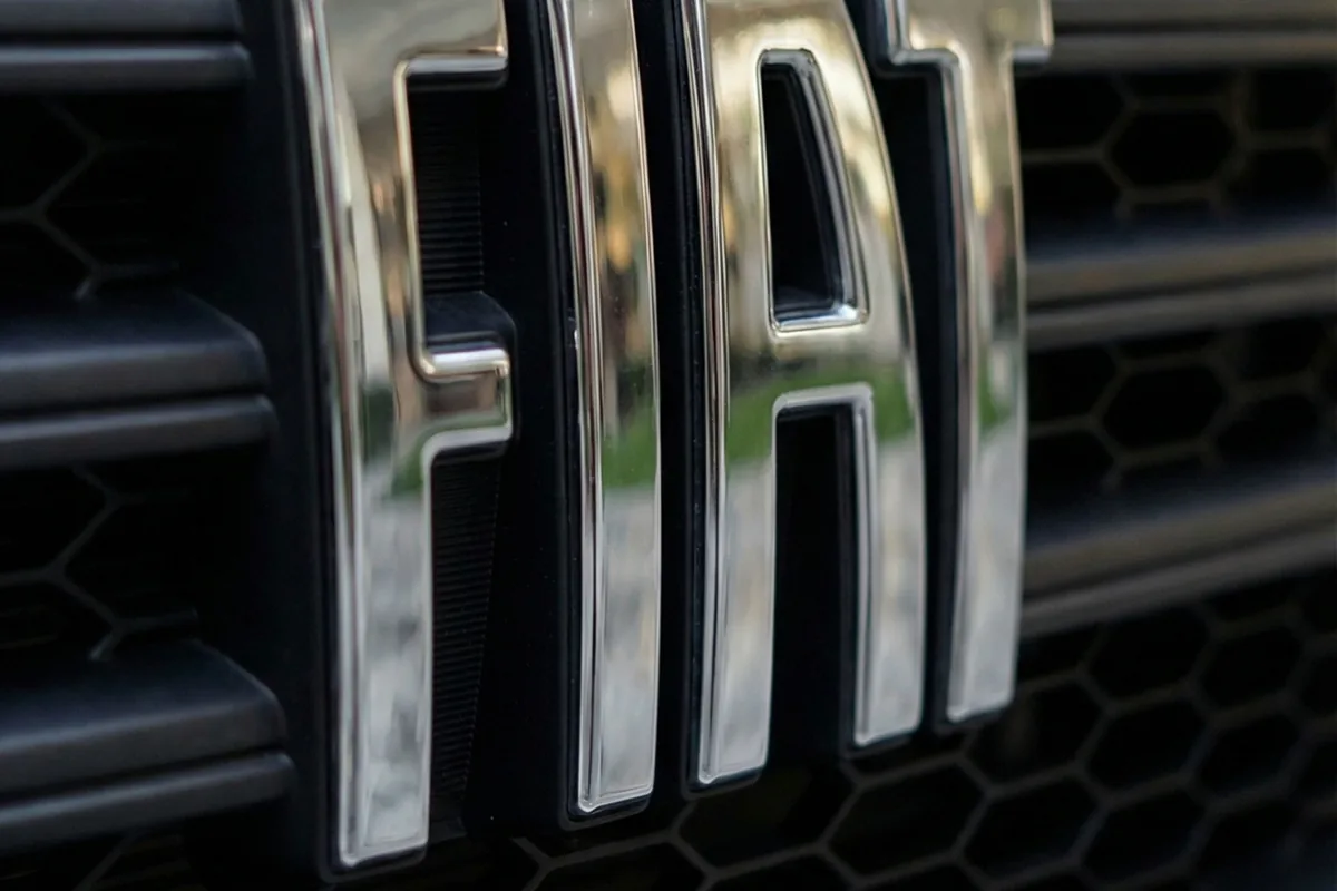 Letras FIAT vazadas em metal escovado sobre a grade colmeia escura da Fiorino conceito.