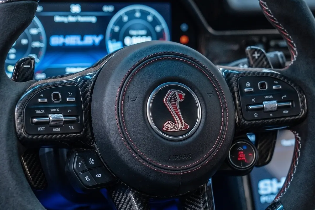 Volante de aro achatado com emblema da cobra ao centro e painel digital azul atrás, no Corcel conceito.