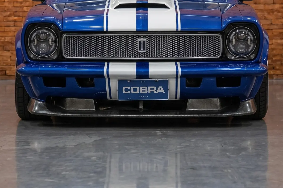 Vista frontal reta do Ford Corcel Shelby, com faróis redondos duplos e faixas brancas paralelas no capô.