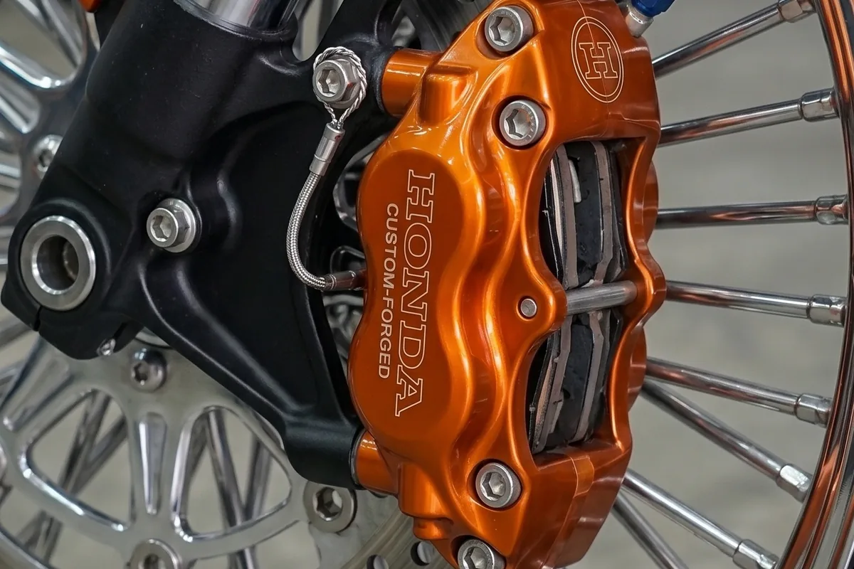 Freio dianteiro do conceito com pinça usinada laranja escrita Honda Custom Forged e disco perfurado.