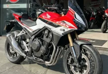 Honda CBX 750F Hollywood: o retorno da Sete Galo, recriado com IA Honda CBX 750F em conceito digital, com pintura vermelha e branca, parada na calçada em frente a uma loja.
