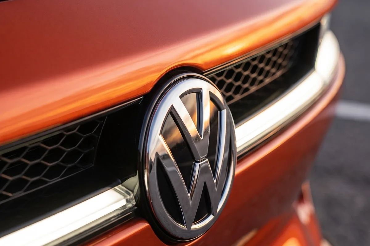Close da grade frontal do VW SP2 EV laranja com logotipo VW cromado e detalhe da barra de luz horizontal