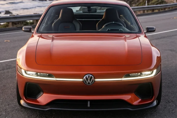 Vista frontal do Volkswagen SP2 EV laranja com faixa de LED e logo VW centralizado, em estrada à beira-mar