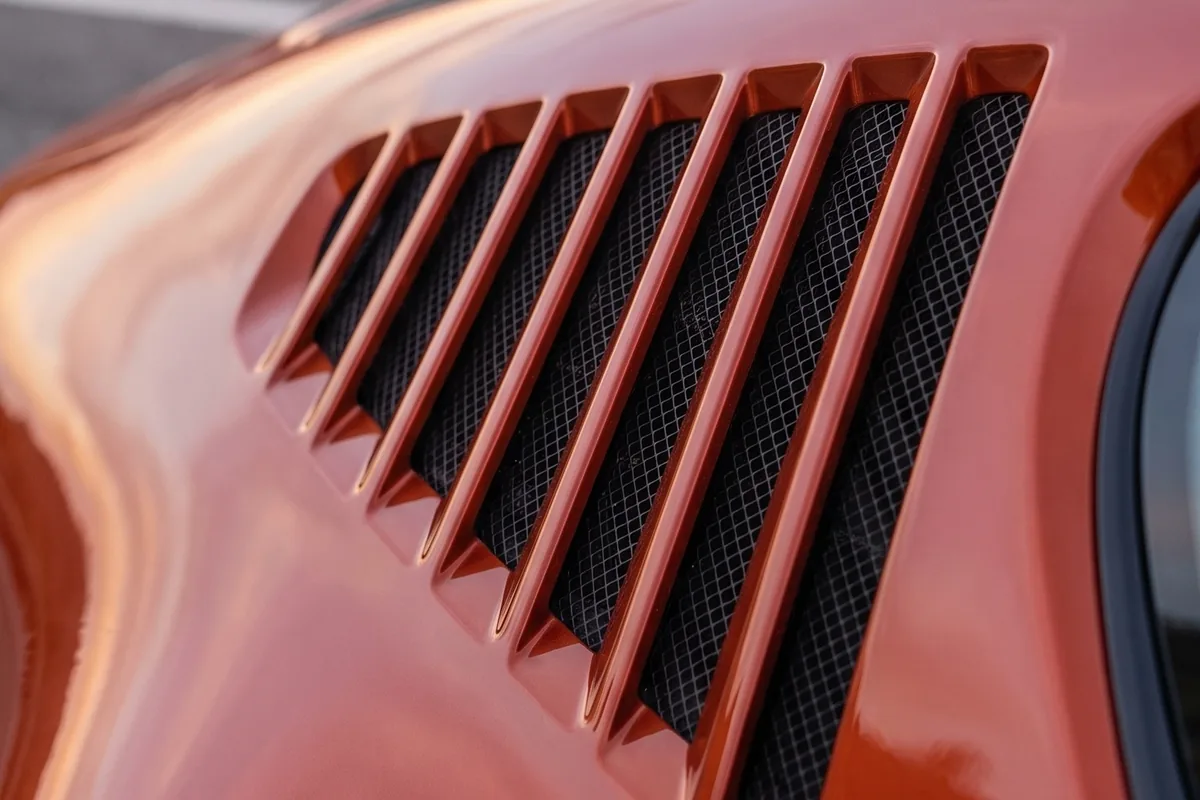 Close das saídas de ar laterais do VW SP2 EV em laranja, com lâminas diagonais e tela metálica preta