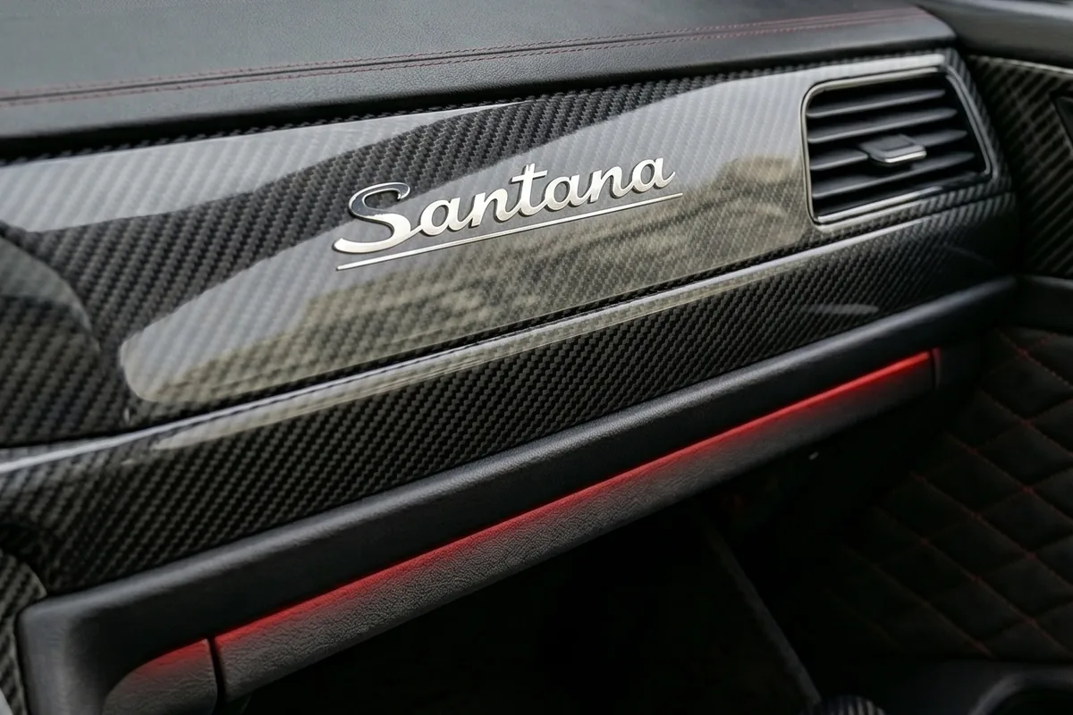 Painel do lado do passageiro com o nome Santana em script cromado sobre fibra de carbono e faixa de luz vermelha.