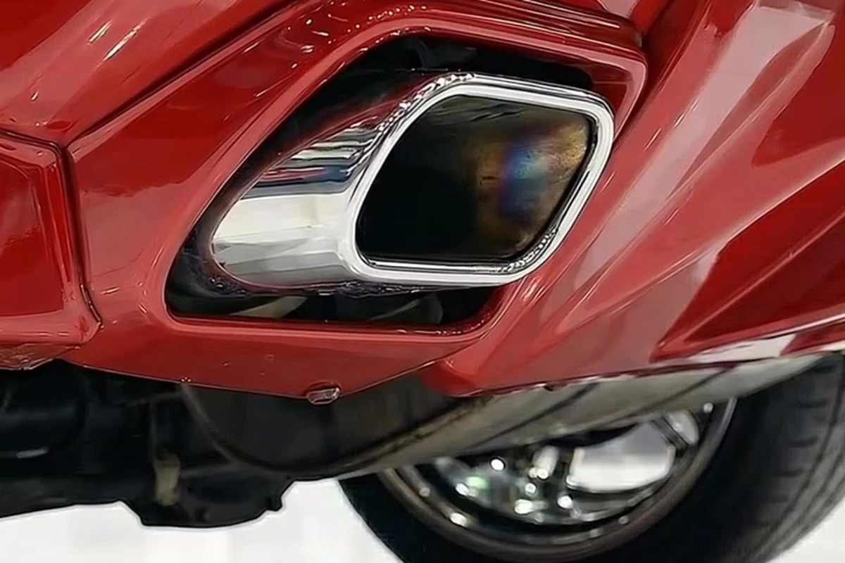 Saída de escapamento traseira cromada integrada ao para-choque vermelho, com a roda aparecendo ao fundo.
